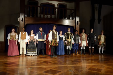 Cast in various costumes lined up at back of wood checkered stage and balcony backdrom