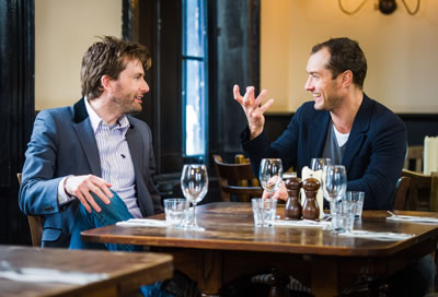 David Tennant and Jude Law (with hand up as if he's holding Yorick's skull) talk at a table in a pub